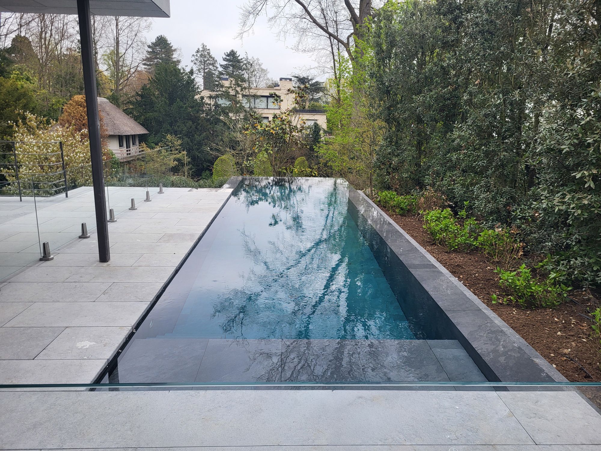 Piscine à débordement en béton à Uccle, eau miroir et pierre sombre
